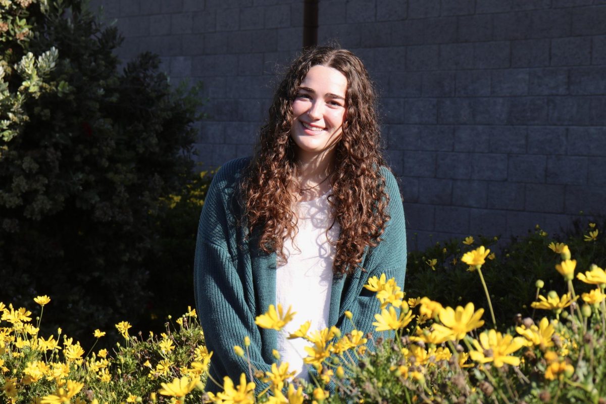Emma Hughes posing with some of the yellow flowers on campus at MBHS.