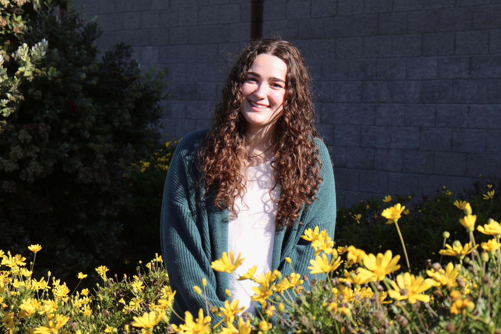 Emma Hughes posing with some of the yellow flowers on campus at MBHS.