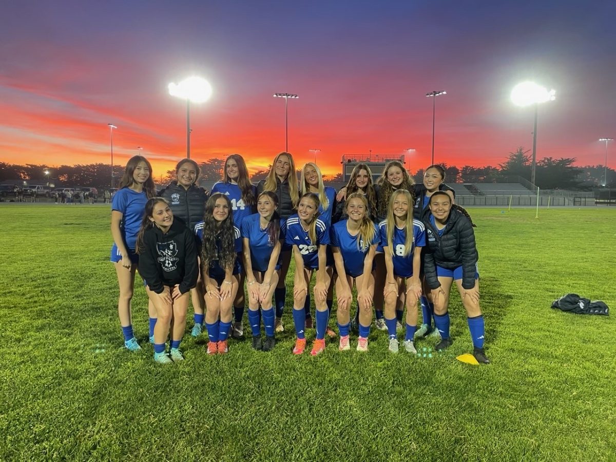 Girls Varsity Soccer team poses in front of sunset before practice.
