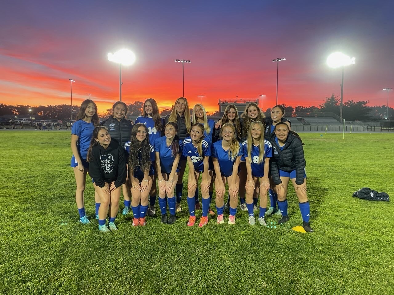 Girls Varsity Soccer team poses in front of sunset before practice.
