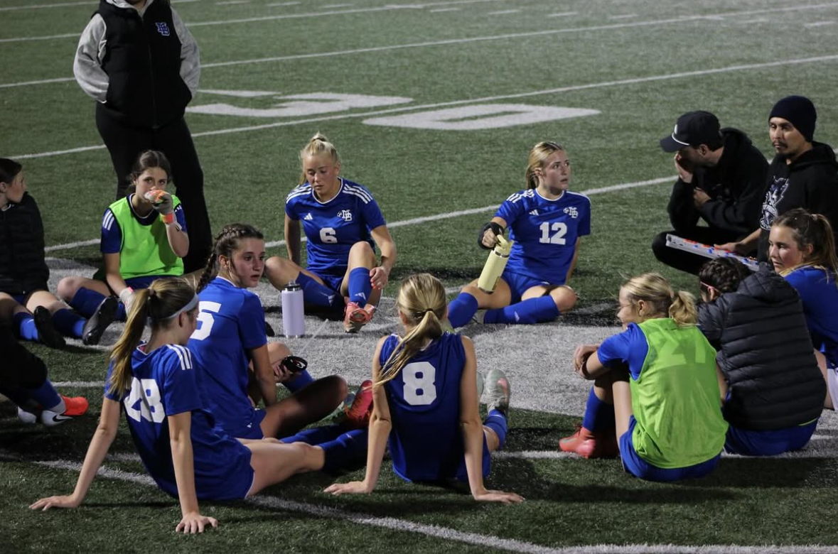 Varsity soccer stretches during halftime while coaches discuss their next steps for the next half. (Source: MBHS girls soccer)