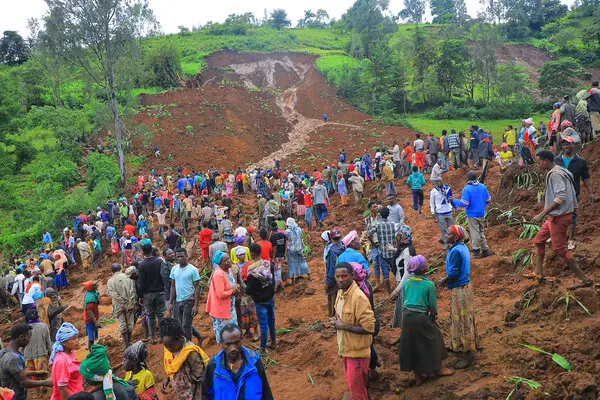 A large group of people gather at a small flood and the start of a landslide. 
