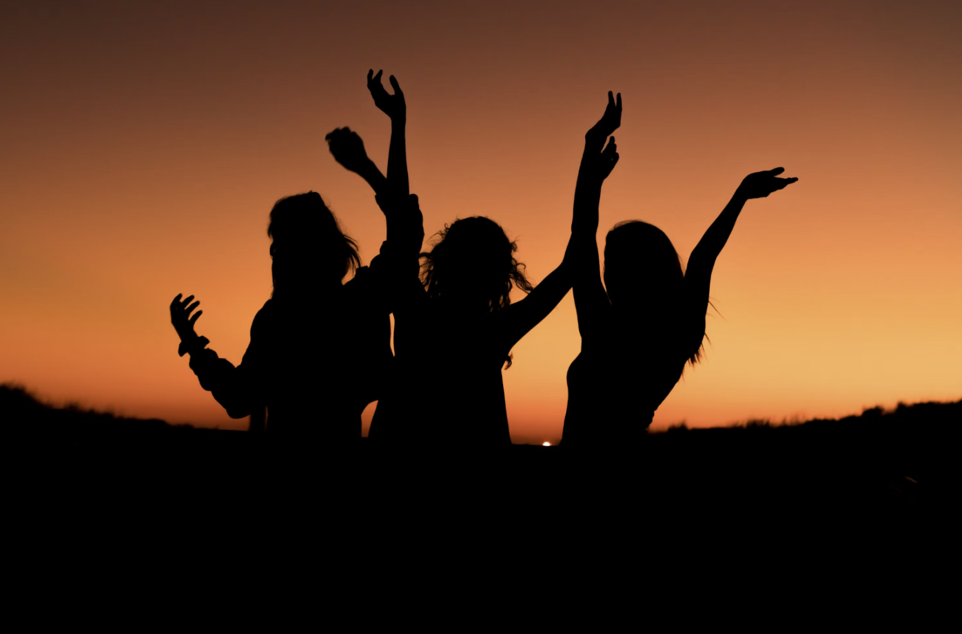 Three girls at sunset, throwing their hands in the air. (Source: Unsplash)